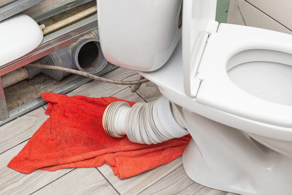 Toilet with a disconnected flexible waste pipe resting on a red cloth on the floor.