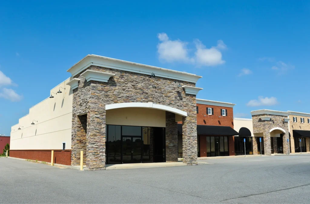 Empty strip mall with stone and brick storefronts under a clear blue sky.