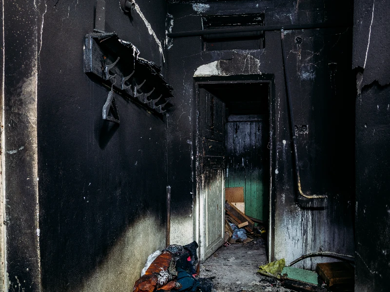 Burned and soot-covered room with an open door leading to a cluttered, damaged interior. fire damage restoration