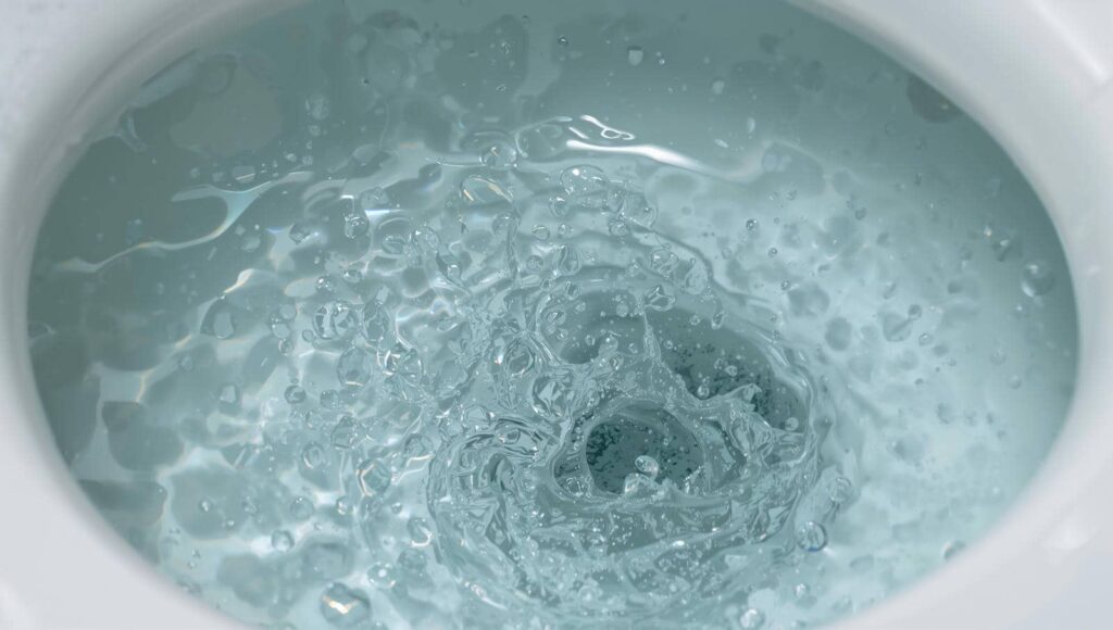 Water swirling and splashing down a toilet bowl drain.