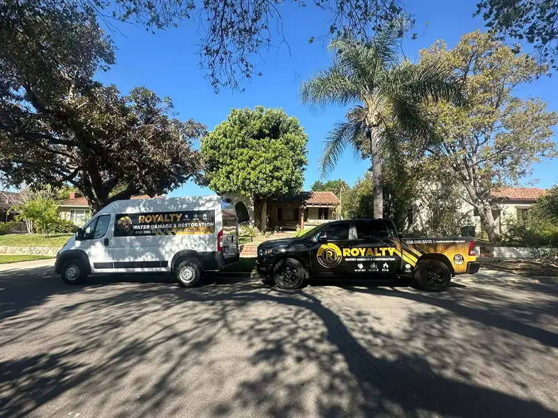 Two Royalty Water Damage & Restoration vehicles parked on a residential street in front of houses. trusted restoration company