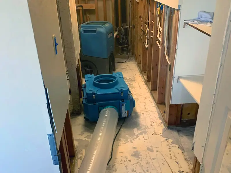 Blue industrial air mover and dehumidifier in a partially gutted room with exposed wall studs. water damage restoration