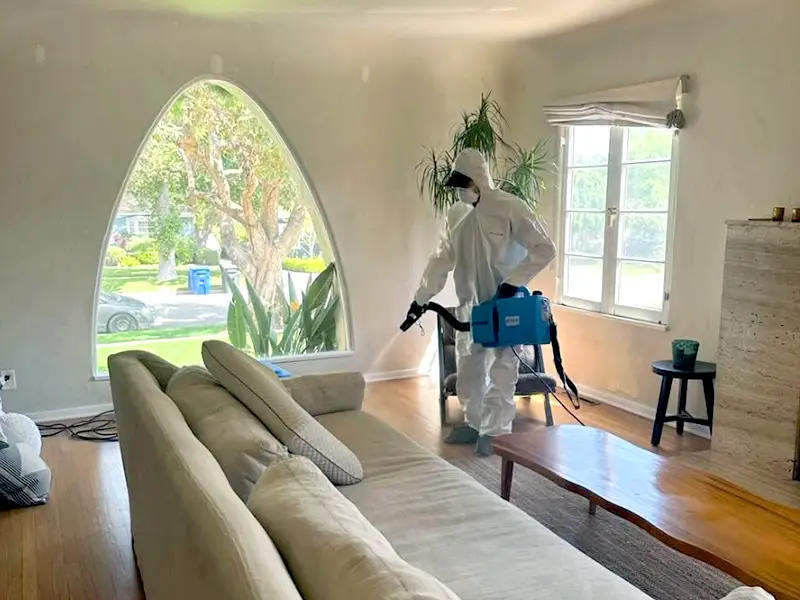 Person in protective suit disinfects a living room with a fogging machine. trusted restoration company