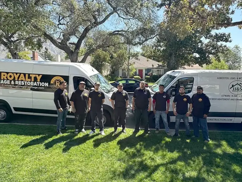 Eight men stand in a row on grass between two white company vans under trees. trusted restoration company