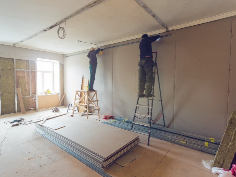 Two workers on ladders installing drywall in a room under construction. reconstruction services